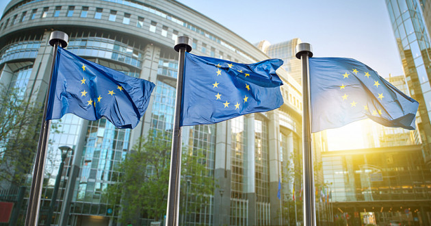 Three European Union (EU) flags in front of a government building in Brussels.