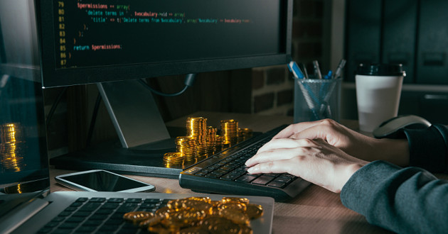 A person writing code with coins on his or her desk.