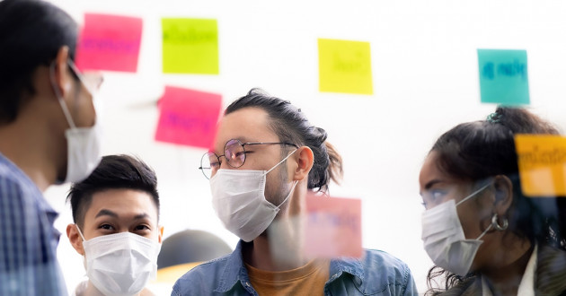 Photo of four employees brainstorming with stickie notes while wearing masks