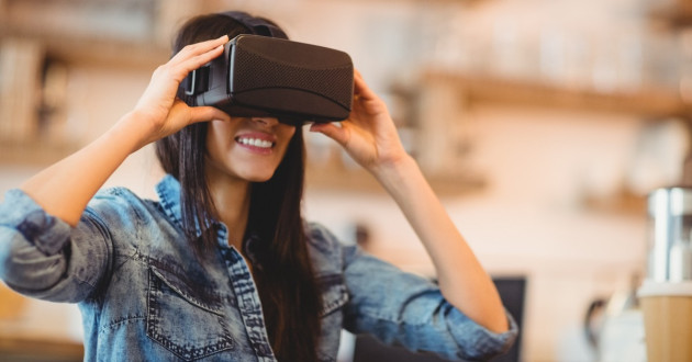A young woman wearing a denim jacket and virtual reality goggles, smiling