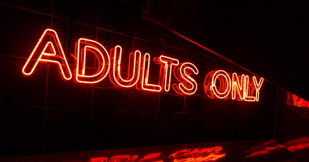 Closeup on a red neon light sign that reads "Adults Only"