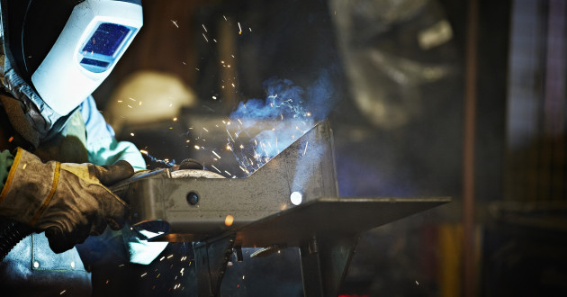 A welder wearing safety helmet, gloves and apron working in a steel manufacturing facility