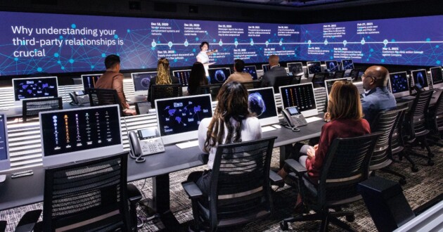 A diverse group of professionals having a discussion in a modern cyber defense office with large digital screen wall