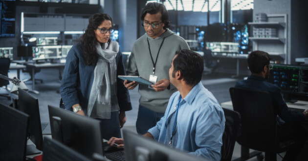 3 Indian IT professionals gathered around a computer in an office having a discussion