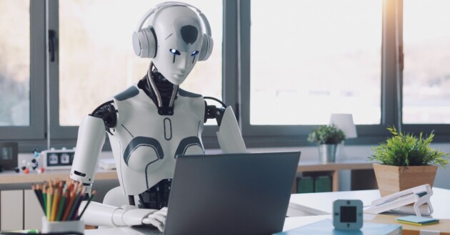 A humanoid robot works in an office on a laptop wearing headphones