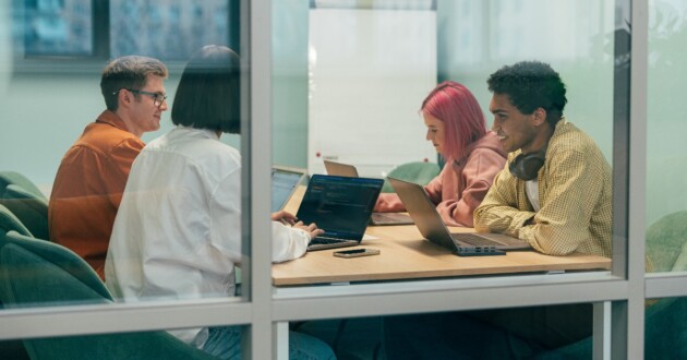 Looking into a conference room at people sitting at a table talking through a window