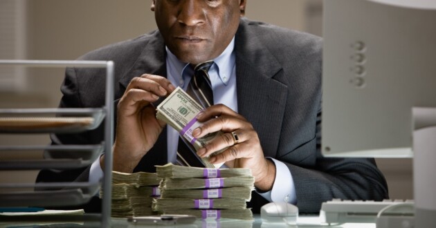 An African businessman sitting at a desk counting a stack of money