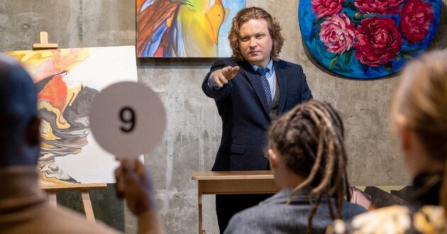 Mature man in suit leading an auction pointing at man with his numbered paddle raised