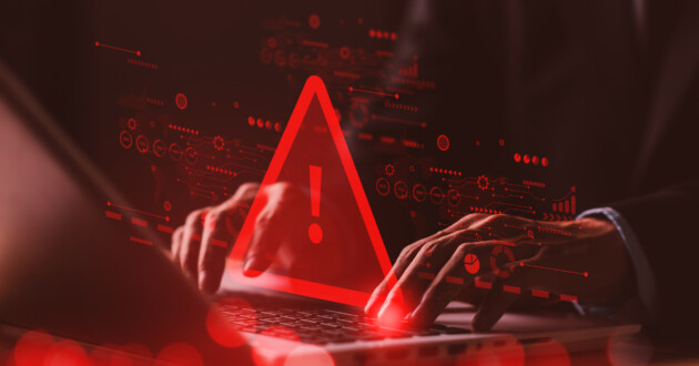 Hands typing on a laptop with a digital red warning icon projecting over the hands