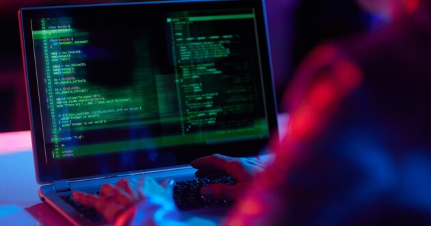 Closeup on a laptop screen displaying green code in a dimly red-lit room